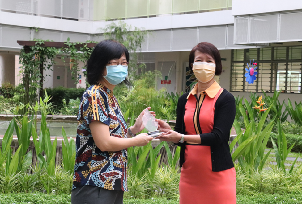 A teacher receiving the TKGS Caring Teacher Award from Principal in the school courtyard.